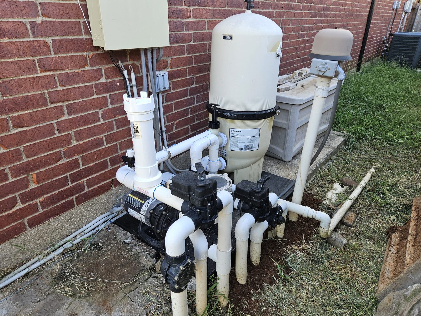 Pool equipment pad with a pump and filter installed against a brick wall