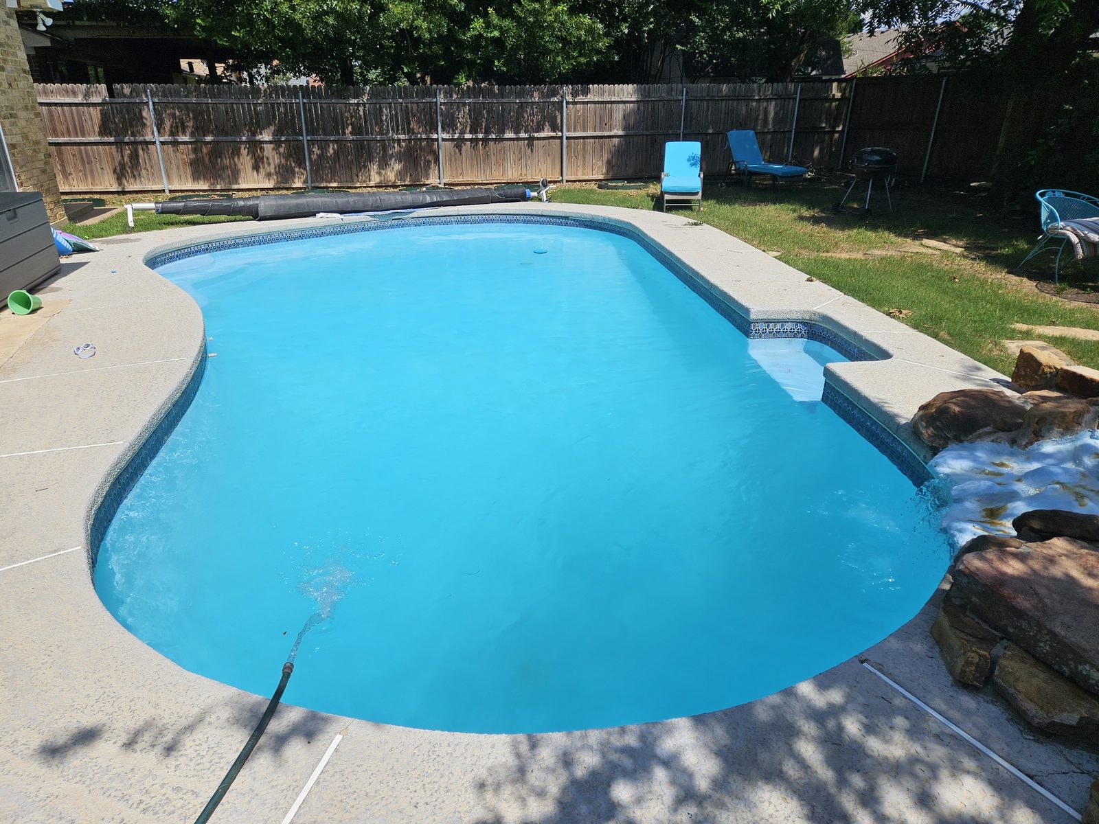 Freeform pool with a rock waterfall and clear blue water in a landscaped backyard
